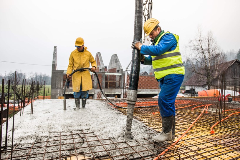Construction workers pouring concrete over reinforced steel rebar on a building site.