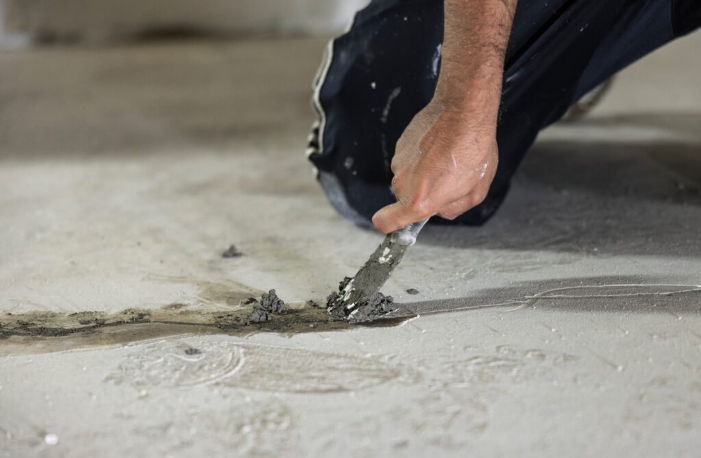 Worker repairing cracks in a concrete floor using a trowel and patching compound.