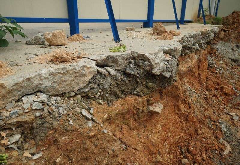 Damaged concrete slab with exposed soil and broken near a building foundation in Texas & Louisiana