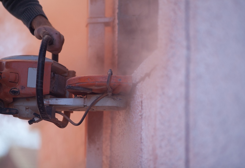 Handheld concrete saw cutting through a concrete wall, creating dust in Texas & Louisiana
