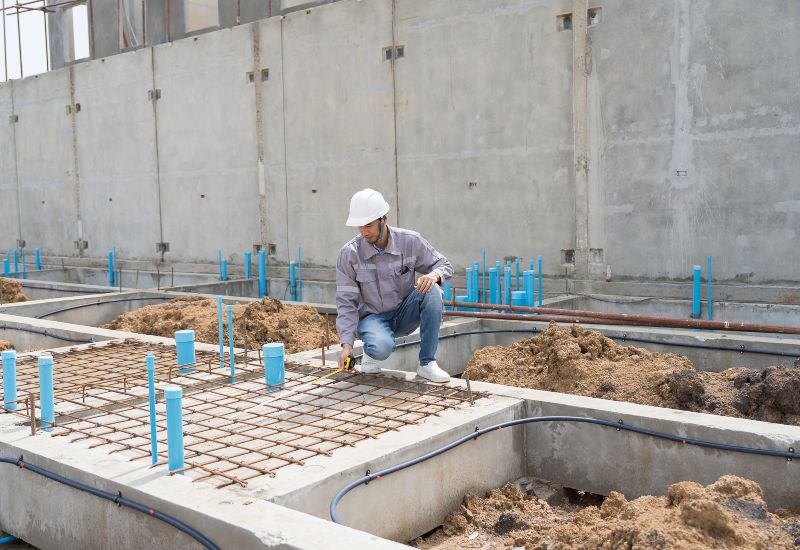 Construction worker measuring rebar grid in concrete foundation trenches in Texas & Louisiana